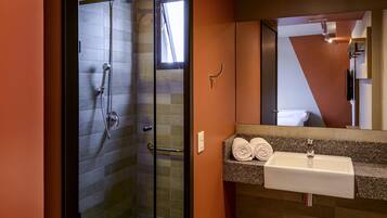 Un baño moderno con ducha de vidrio, lavamanos con encimera de granito y un espejo grande.