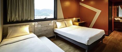 Habitación de hotel con dos camas, una ventana con cortinas, un escritorio con lámpara y vistas a las montañas.
