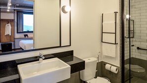 A modern bathroom with a large mirror, a sink, a toilet, and a shower area.