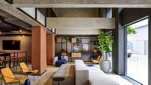 A modern lounge area with seating arrangements, a bar, and a large window providing a view of the street. - Ibis Plaza Balneario Camboriu (Balneário Camboriú)