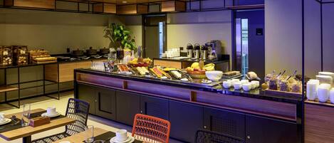 Um buffet de café da manhã moderno com diversas opções de comida, um espaço para café e diferentes arranjos de assento.