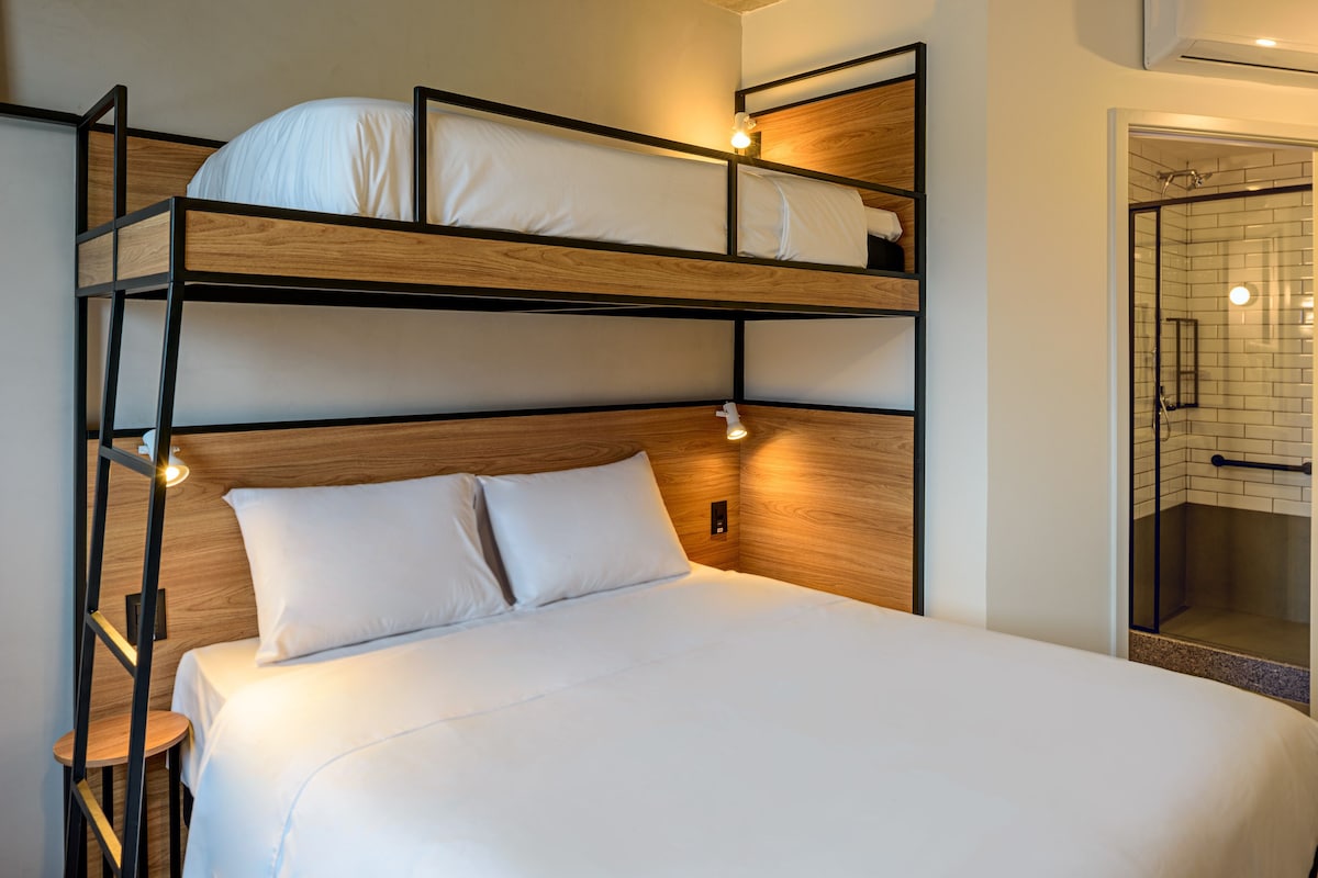 Una cama litera con dos plazas, cabecera de madera y lámparas de noche.