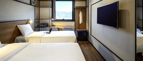Habitación de hotel con dos camas, un escritorio con silla, televisor montado en la pared y ventana con vistas.