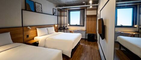 Habitación de hotel con dos camas, piso de madera, un ventanal grande y un televisor.