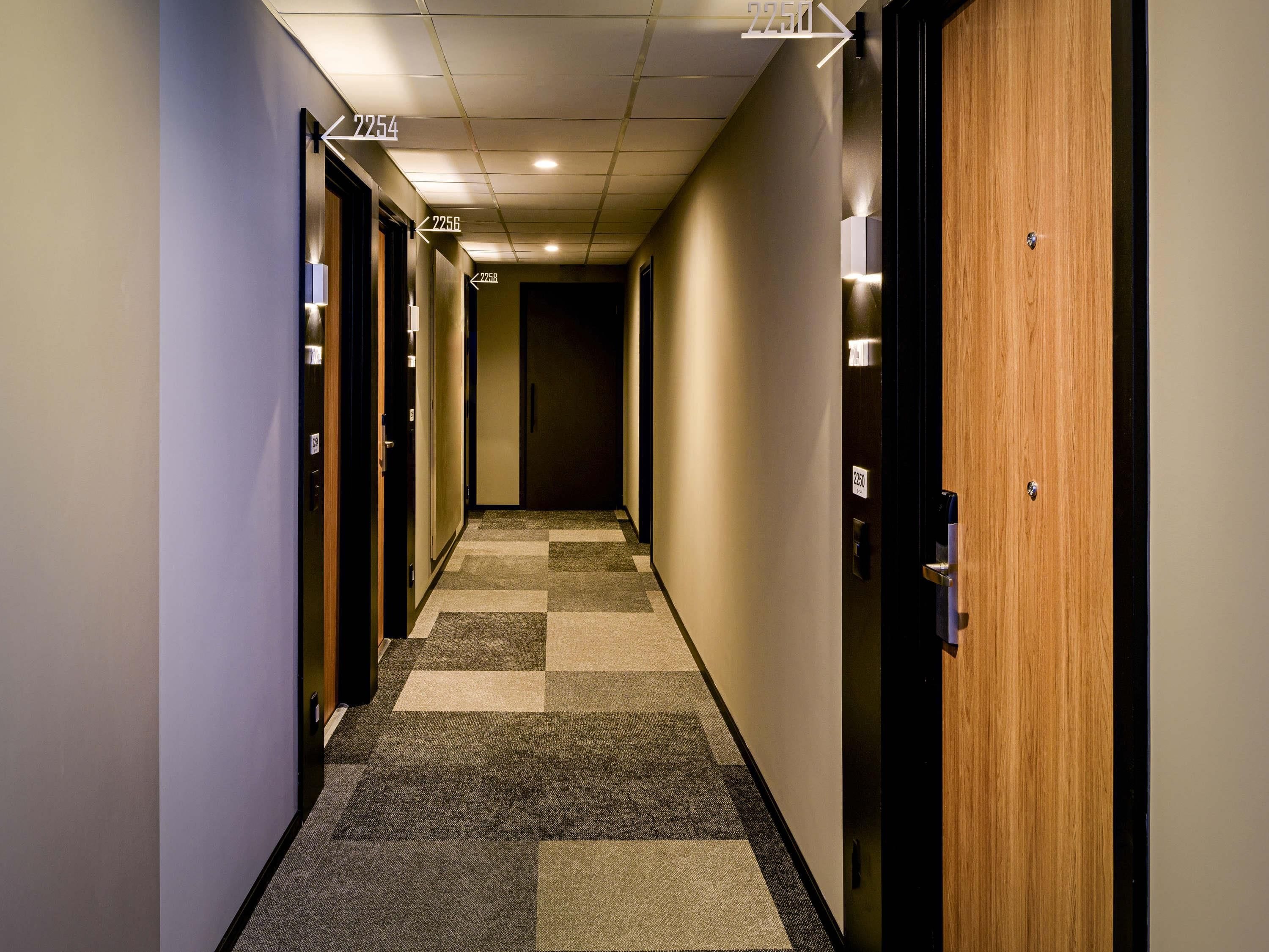 Corredor de hotel com piso carpete, portas numeradas 2254, 2256 e 2258, e uma porta de madeira no lado direito.
