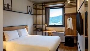 A hotel room with a large bed, a desk with a computer, a TV, and a view of a mountain.