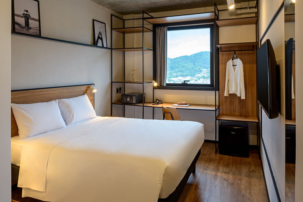 Habitación de hotel con una cama grande, un escritorio con una computadora, un televisor y vistas a la montaña.