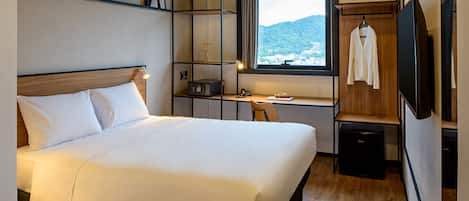 A hotel room with a large bed, a desk with a computer, a TV, and a view of a mountain.