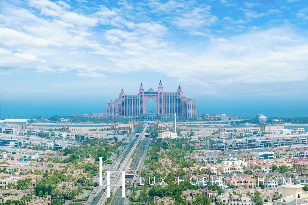 A large hotel with a prominent archway, multiple towers, and a view of the surrounding cityscape and coastline.