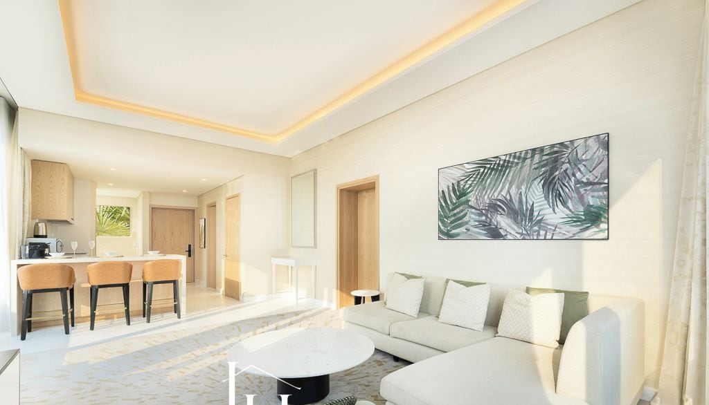 A modern living room with a sofa, coffee table, and artwork. A kitchen with bar stools is visible in the background.