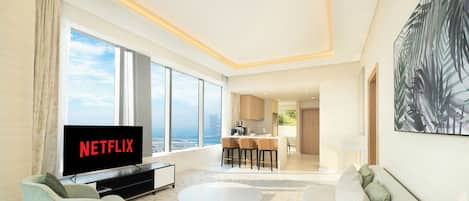 A modern living room with a flat-screen TV, a sofa, a coffee table, and a dining area with chairs.