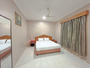 Een hotelkamer met een groot bed, een plafondventilator, een nachtkastje met lamp en een gordijn voor het raam.