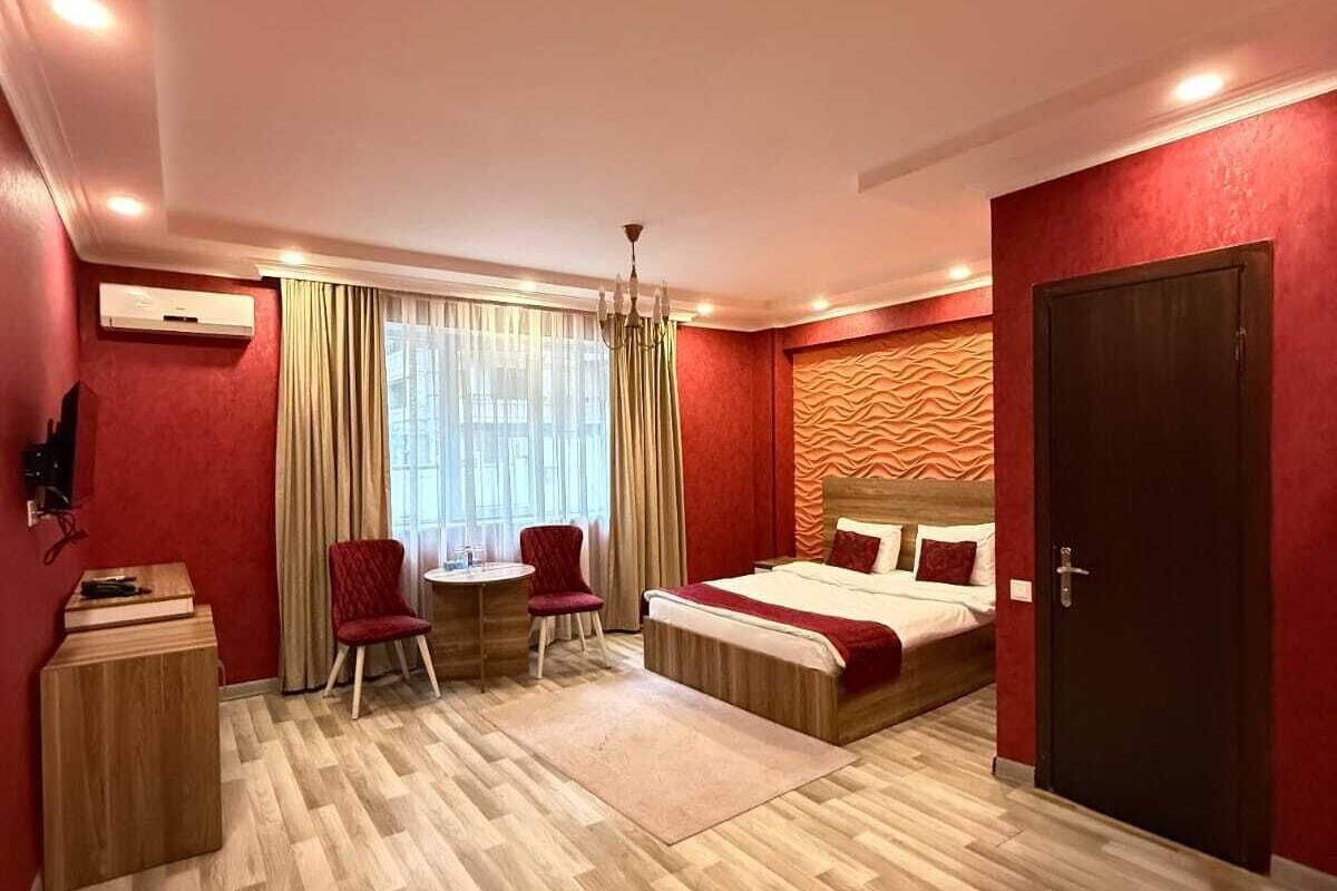 A hotel room with a bed, a desk, two chairs, a wardrobe, and a window with curtains.