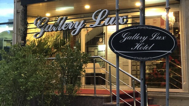 The exterior of Gallery Lux Hotel with a prominent red 'HOTEL' sign, a black awning with the hotel's name, and a staircase leading to the entrance.
