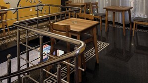 A hotel lobby with a world map mural, wooden tables and chairs, a staircase with metal railings, and a ceiling light fixture.