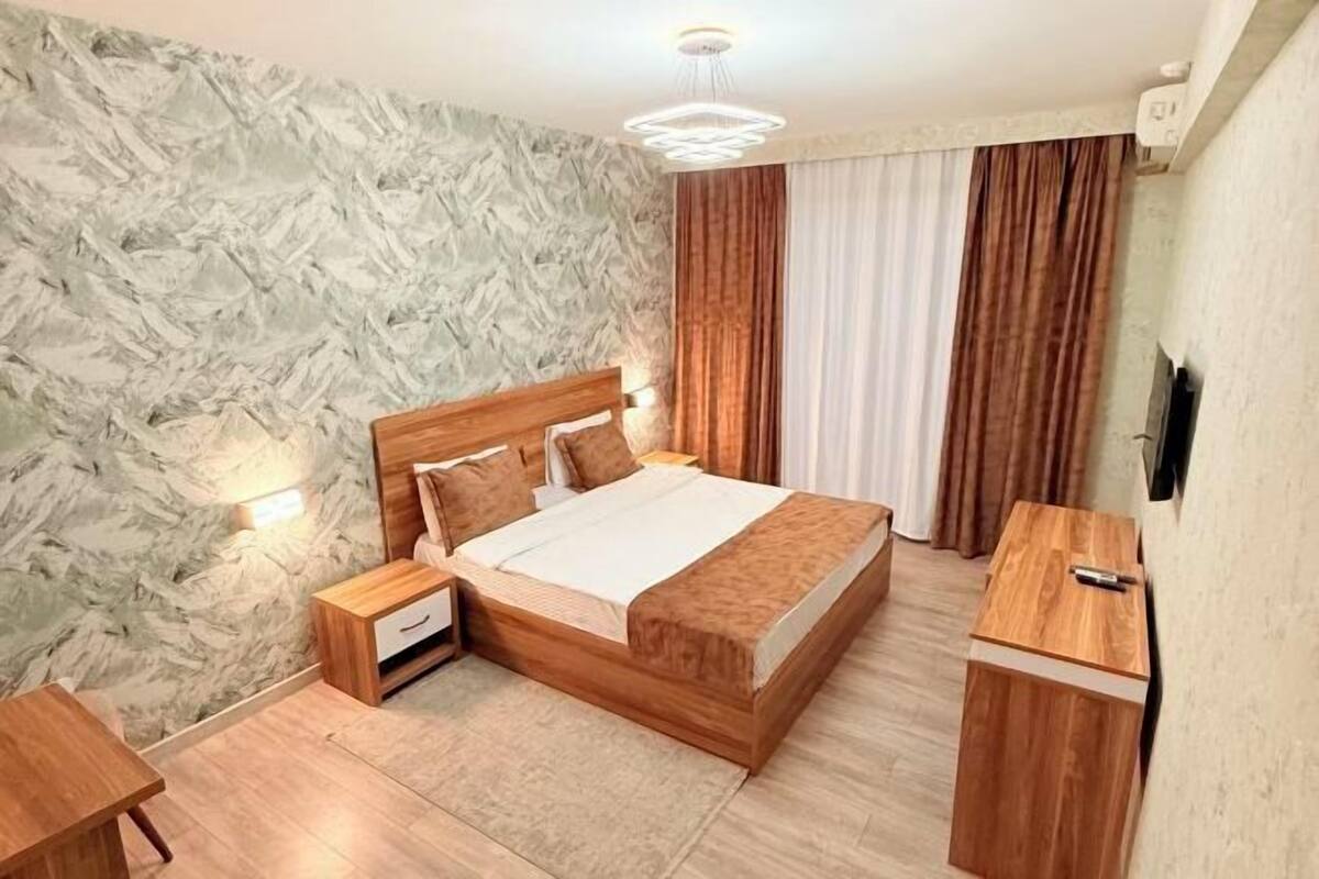 A bedroom with a wooden bed, nightstands, a desk, and a wall-mounted TV.