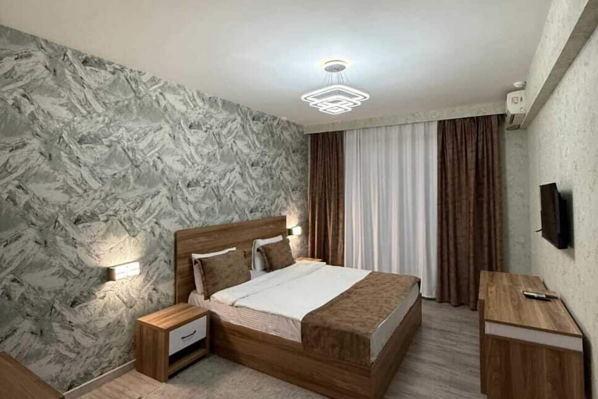 A modern bedroom with a marble-patterned wall, a wooden bed, a desk, and a chair.