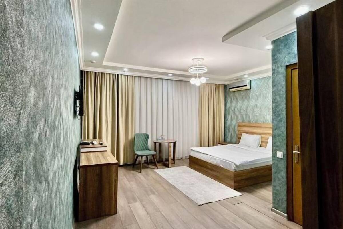A modern hotel room with a wooden bed, a desk, a chair, and a small table.