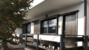 Un bâtiment à l’extérieur blanc, avec des marches en bois menant à un porche et une rambarde en métal.