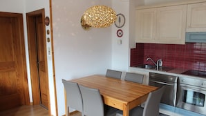 Une cuisine avec une table à manger en bois, des chaises grises, un four en acier inoxydable et un pare-feu rouge en carreaux.