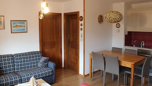 Un salon avec un canapé, une table à manger avec des chaises, des portes en bois et un coin cuisine.