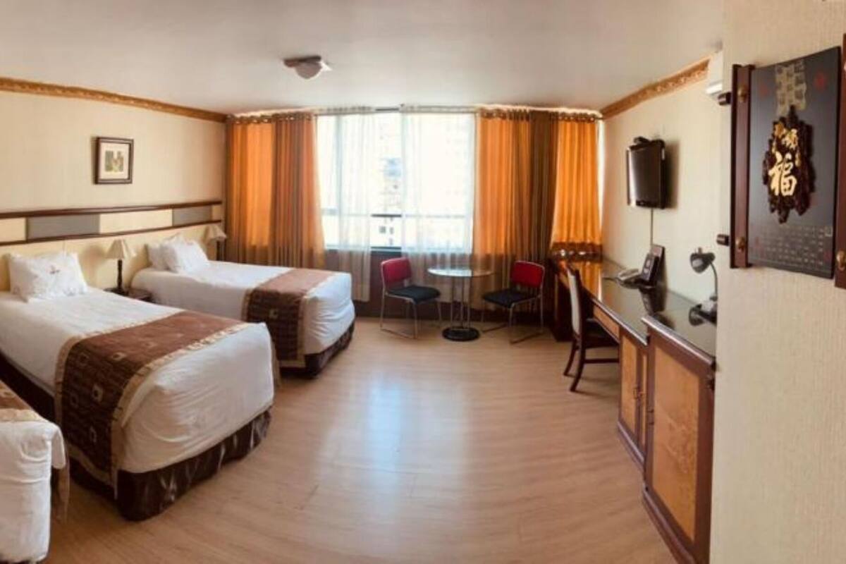 A hotel room with three beds, a desk with a chair, a television, and a window with curtains.