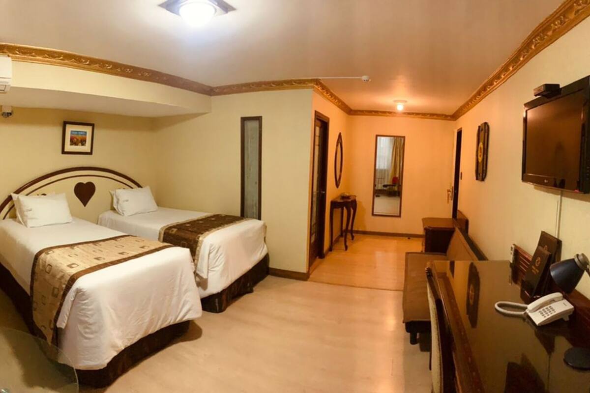 A hotel room with two beds, a desk, a chair, a TV, and a telephone.