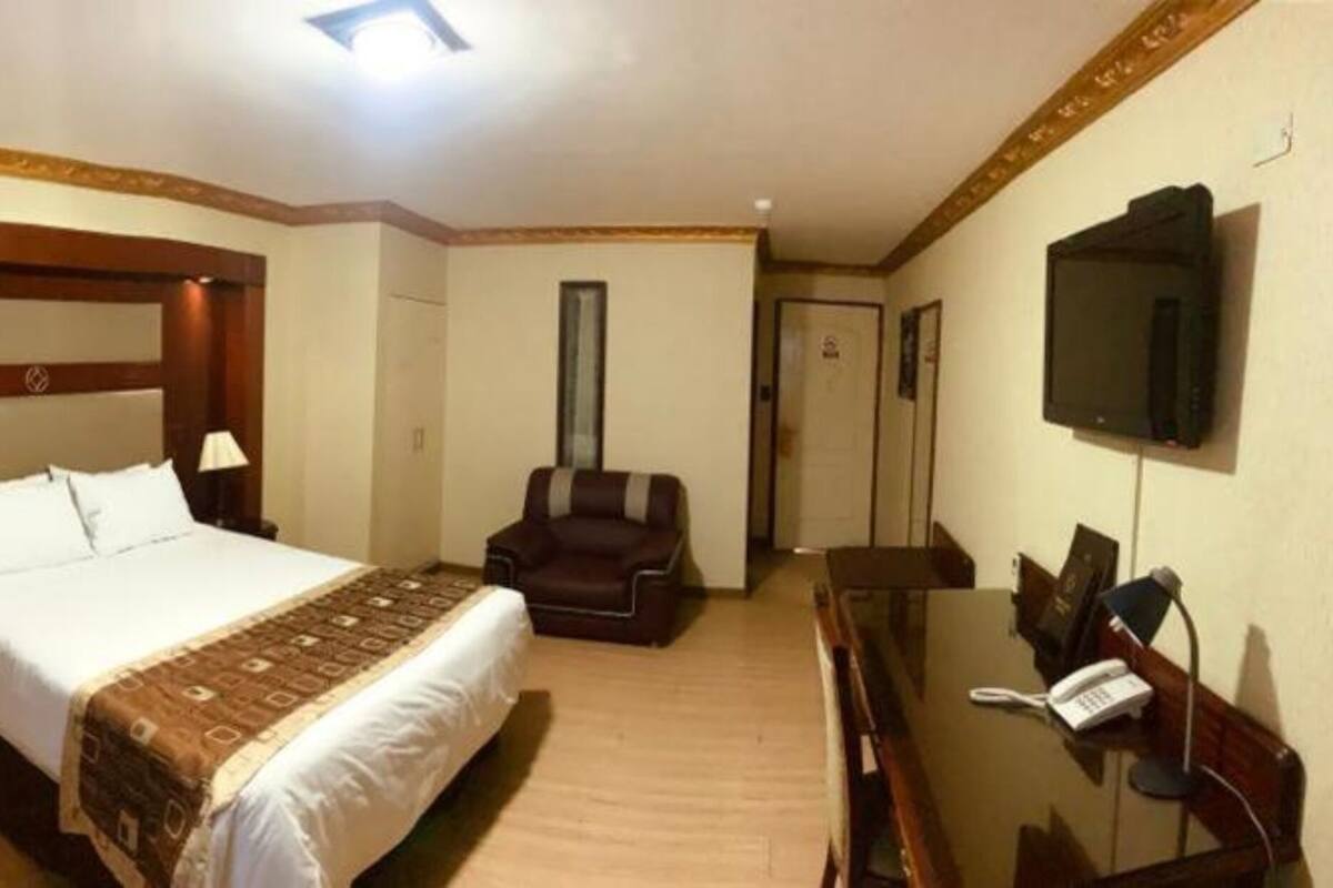 A hotel room with a large bed, a desk with a telephone, a chair, and a television on the wall.