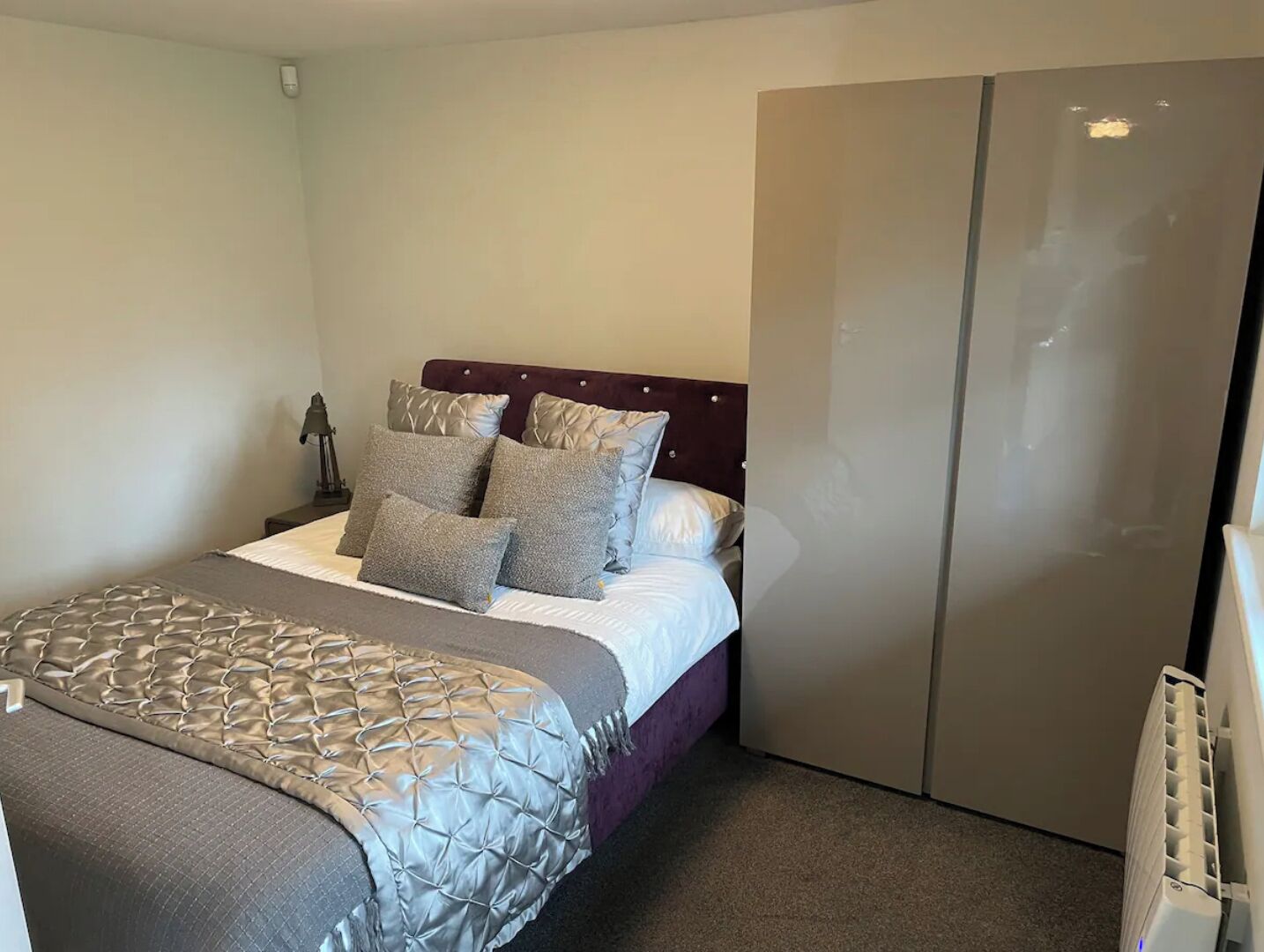 Een slaapkamer met een bed, kussens, een nachtkastje en een kledingkast.