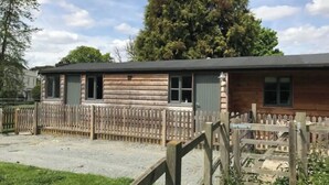 A wooden building with a fenced yard, a gravel driveway, and a large tree in the background. - Riverside Stable Cottage, Hunton Yalding Maidstone (Hunton)