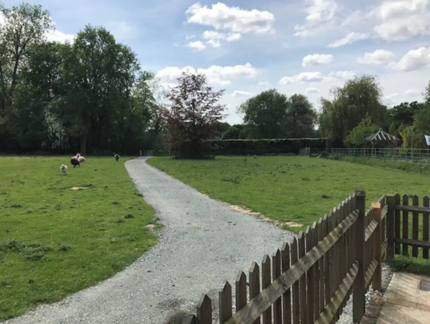 A gravel path leading through a grassy field with a wooden fence on one side.