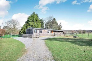 Stable surrounded by a fenced area with a grassy field and trees.