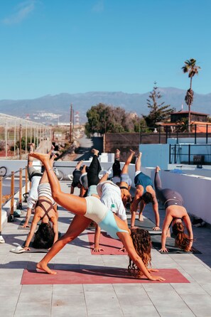 A group of people performing yoga on a rooftop with a cityscape and mountains in the background. - The Tree House Hostel (Granadilla de Abona)