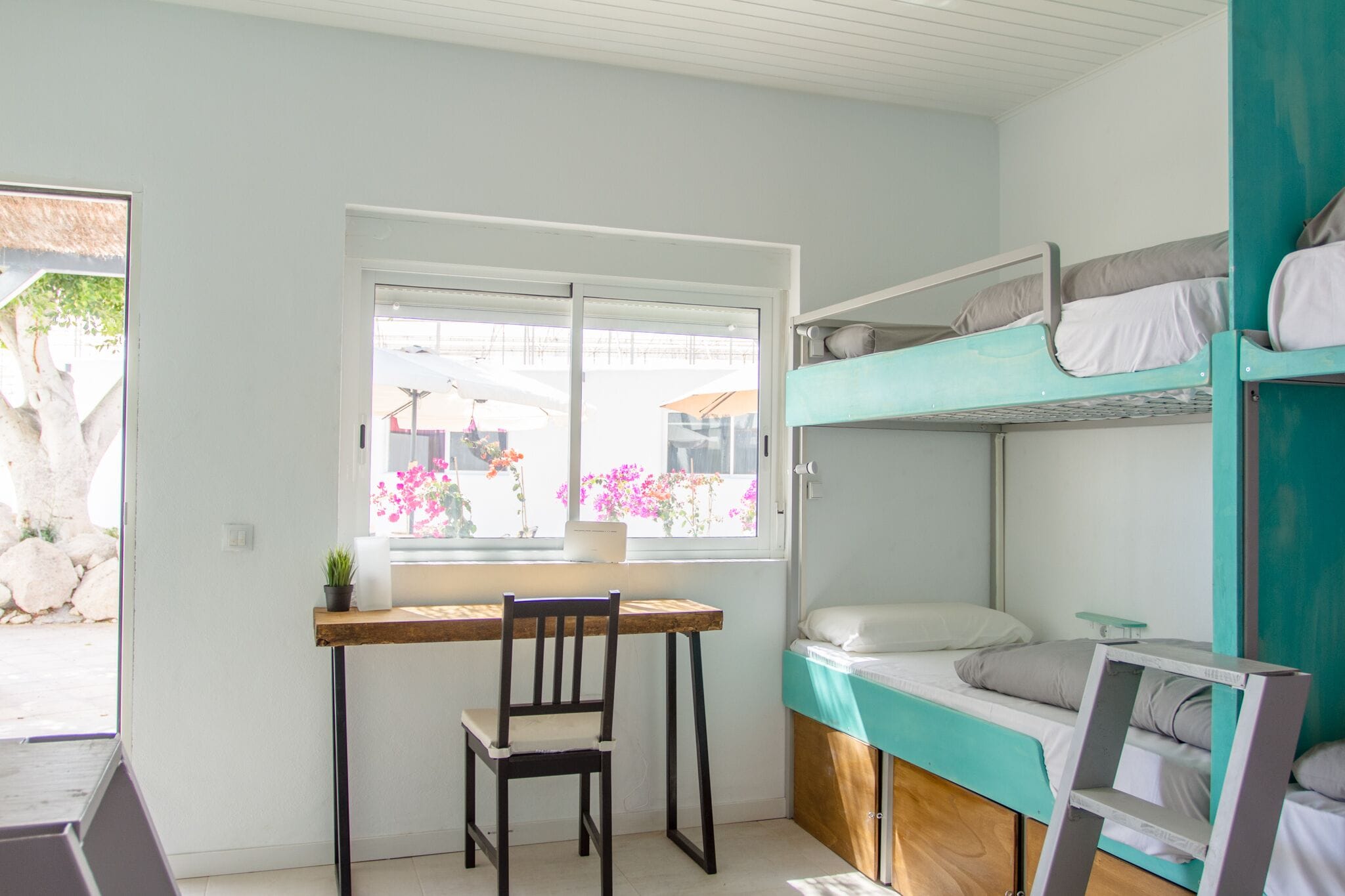 Una habitación pequeña con una cama litera, un escritorio con silla y ventana que da a un jardín.