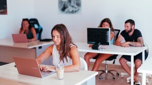 A modern office space with multiple workstations, a white table, and a laptop. - The Tree House Hostel (Granadilla de Abona)