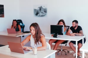 A modern office space with multiple workstations, a white table, and a laptop. - The Tree House Hostel (Granadilla de Abona)