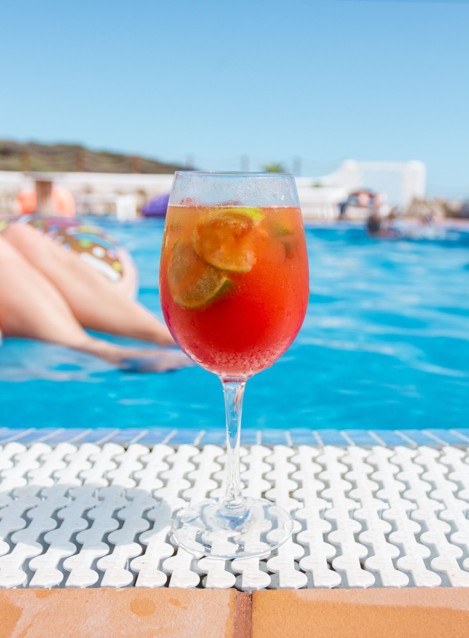 A glass of red drink with lime slices on a white poolside table.