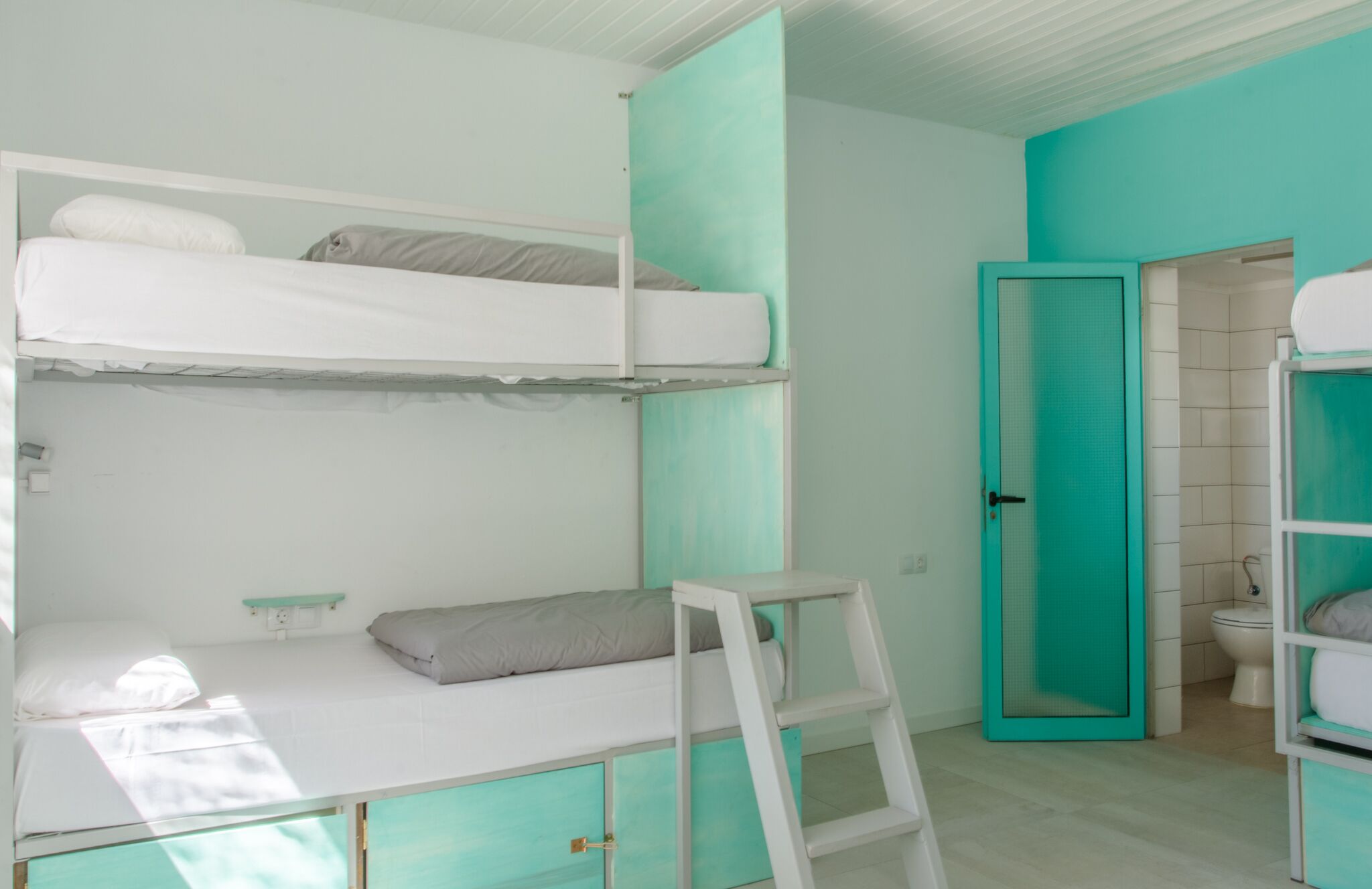 Une chambre avec un lit superposé, une échelle, une petite table et une porte donnant sur une salle de bain.