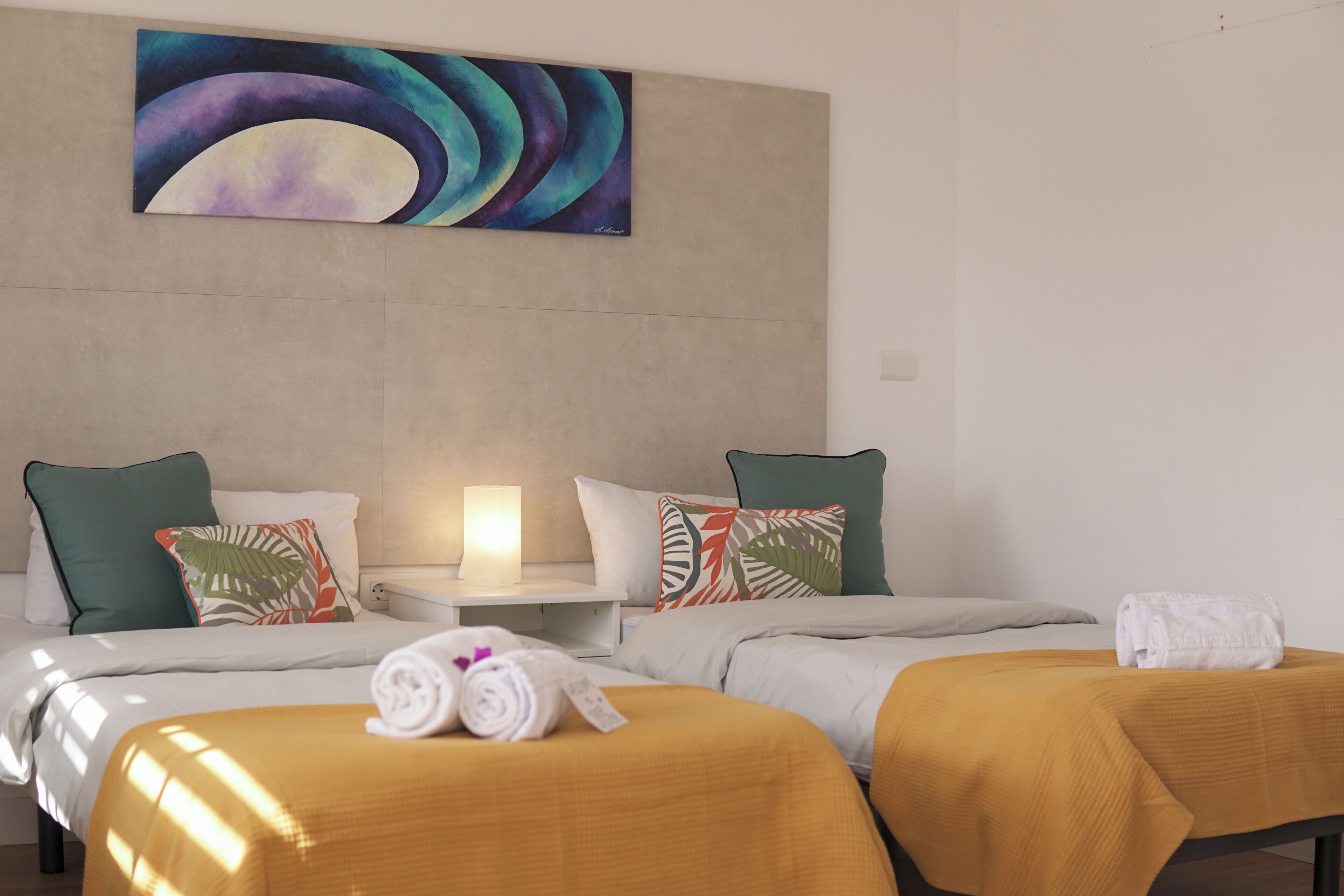Una habitación de hotel con dos camas, una mesita de noche, una lámpara y un cuadro en la pared.