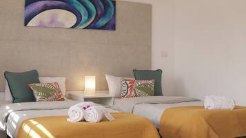 Una habitación de hotel con dos camas, una mesita de noche, una lámpara y un cuadro en la pared.