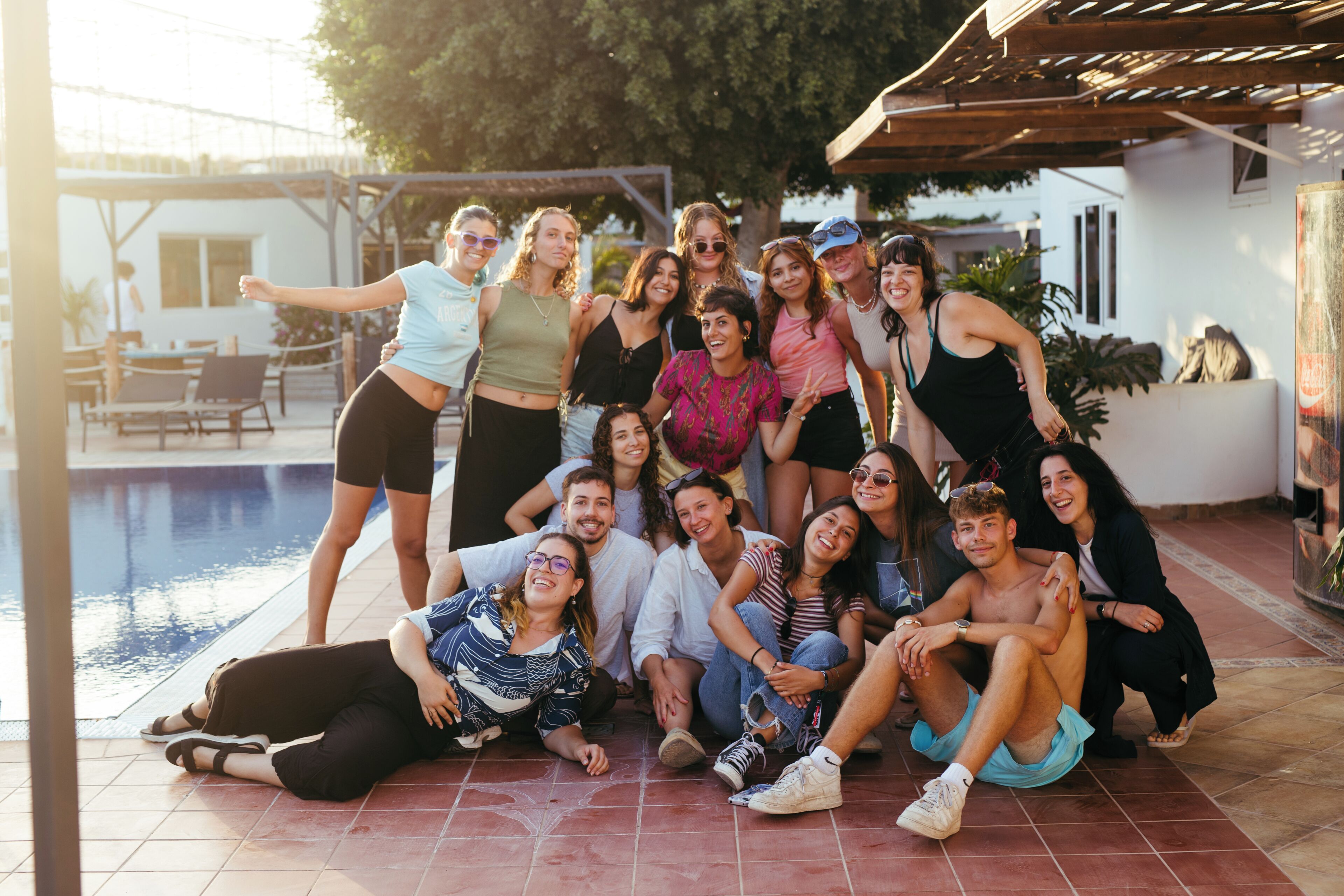 A group of people gathered around a pool area with a pergola overhead.