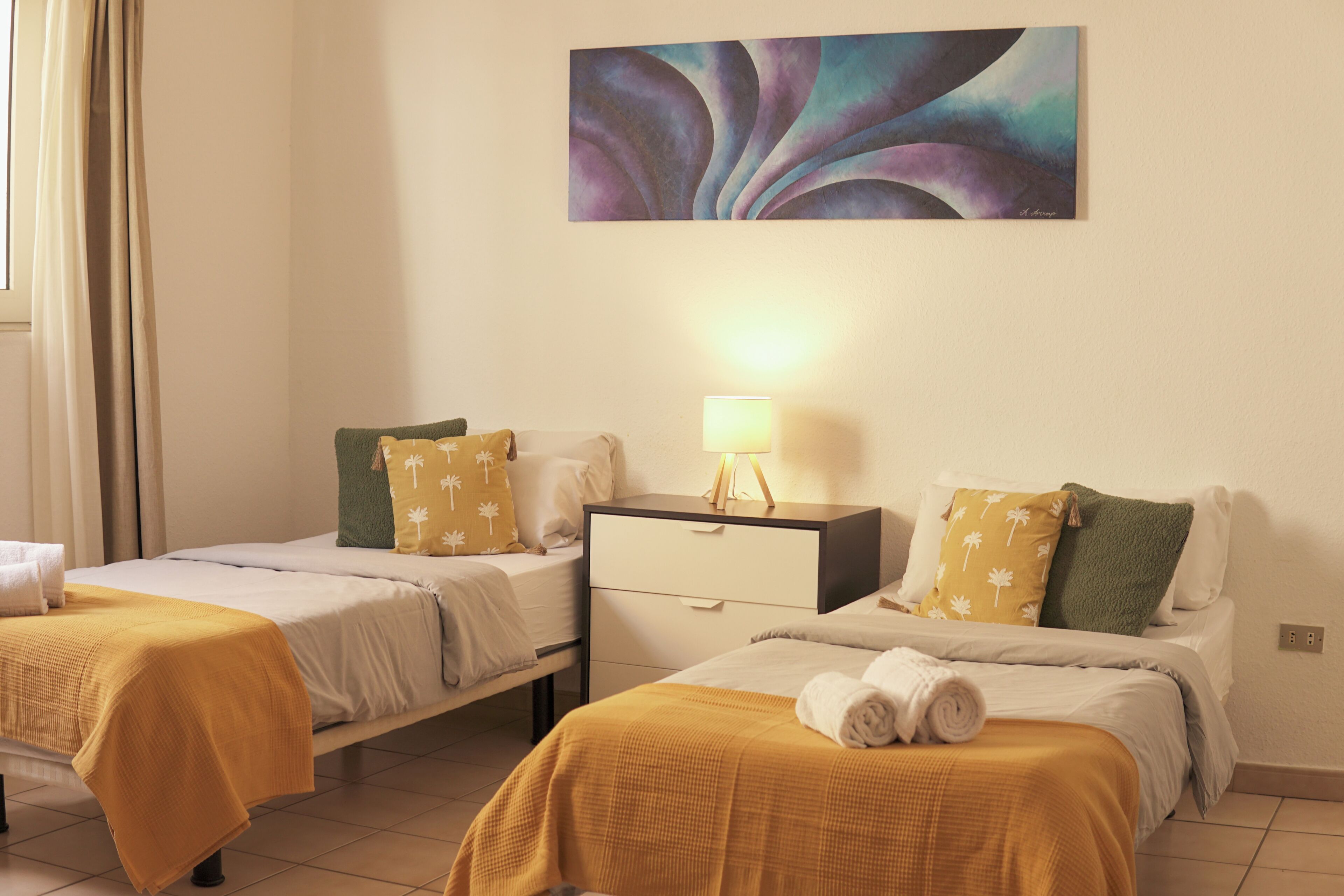 A hotel room with two beds, a nightstand, a lamp, and a painting on the wall.