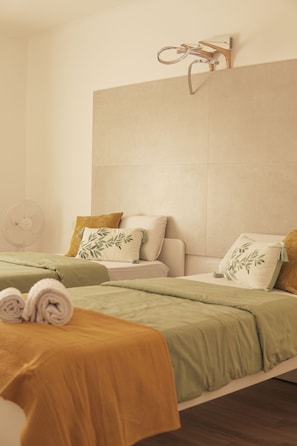 A hotel room with a bed, a bedside table, a fan, and a towel on the floor.