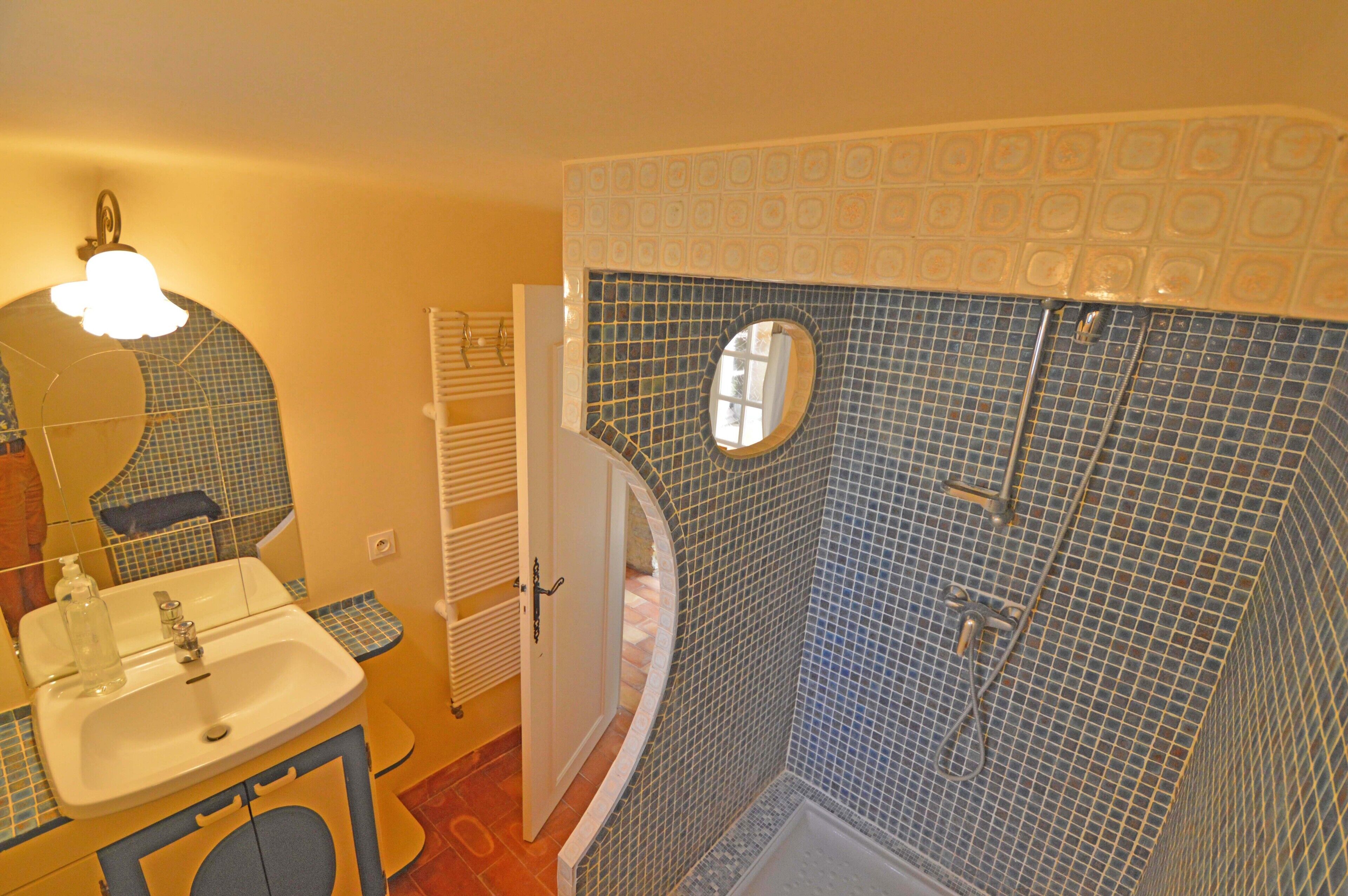 A bathroom with a sink, mirror, and shower area.