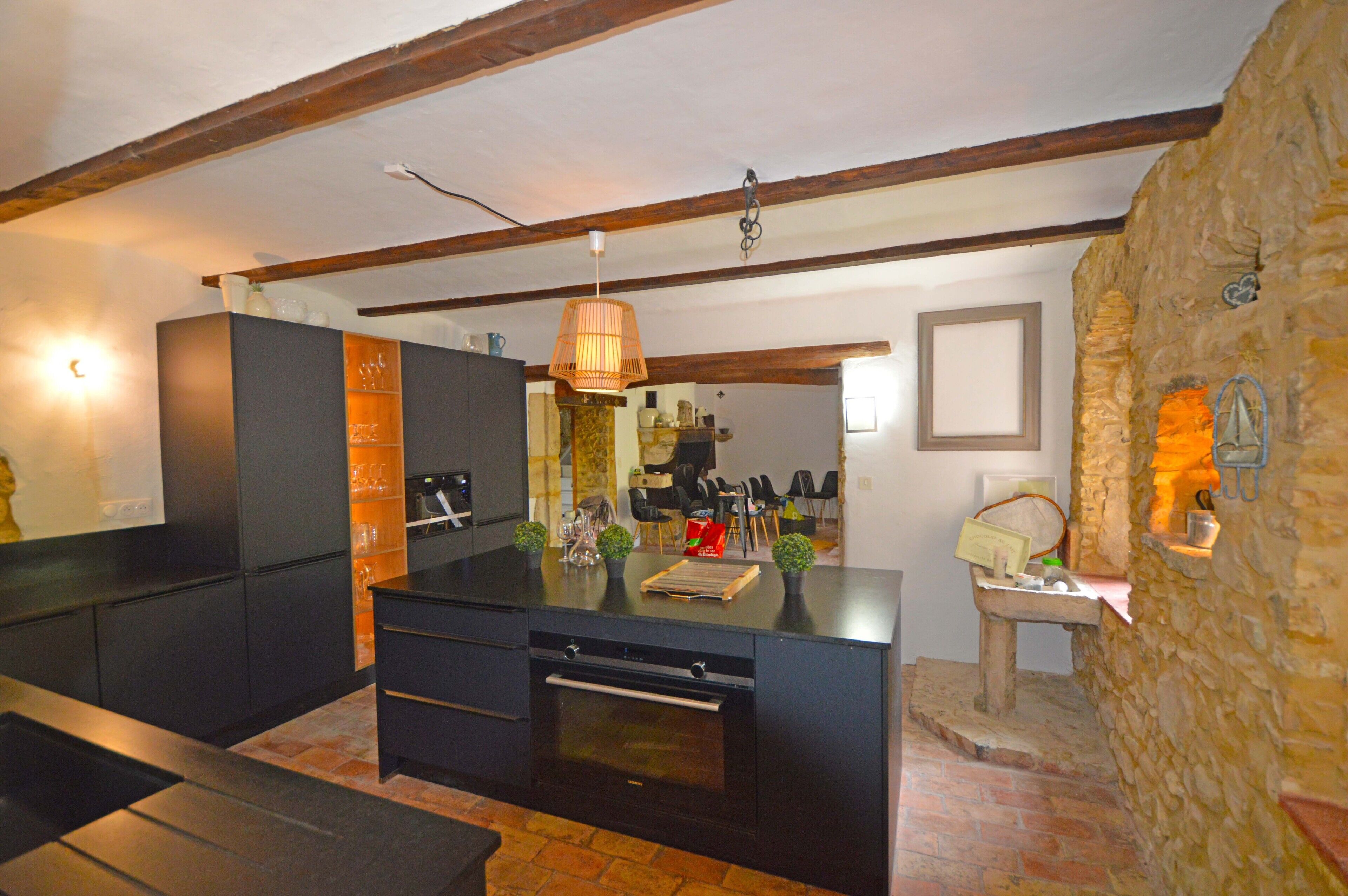 Une cuisine moderne avec des meubles de couleur sombre, un îlot central et un mur d’accent en pierre.