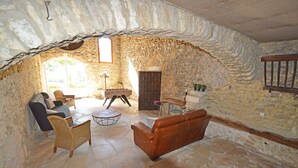 Una habitación de paredes de piedra con chimenea, un sofá, una mesa de centro y una estantería.