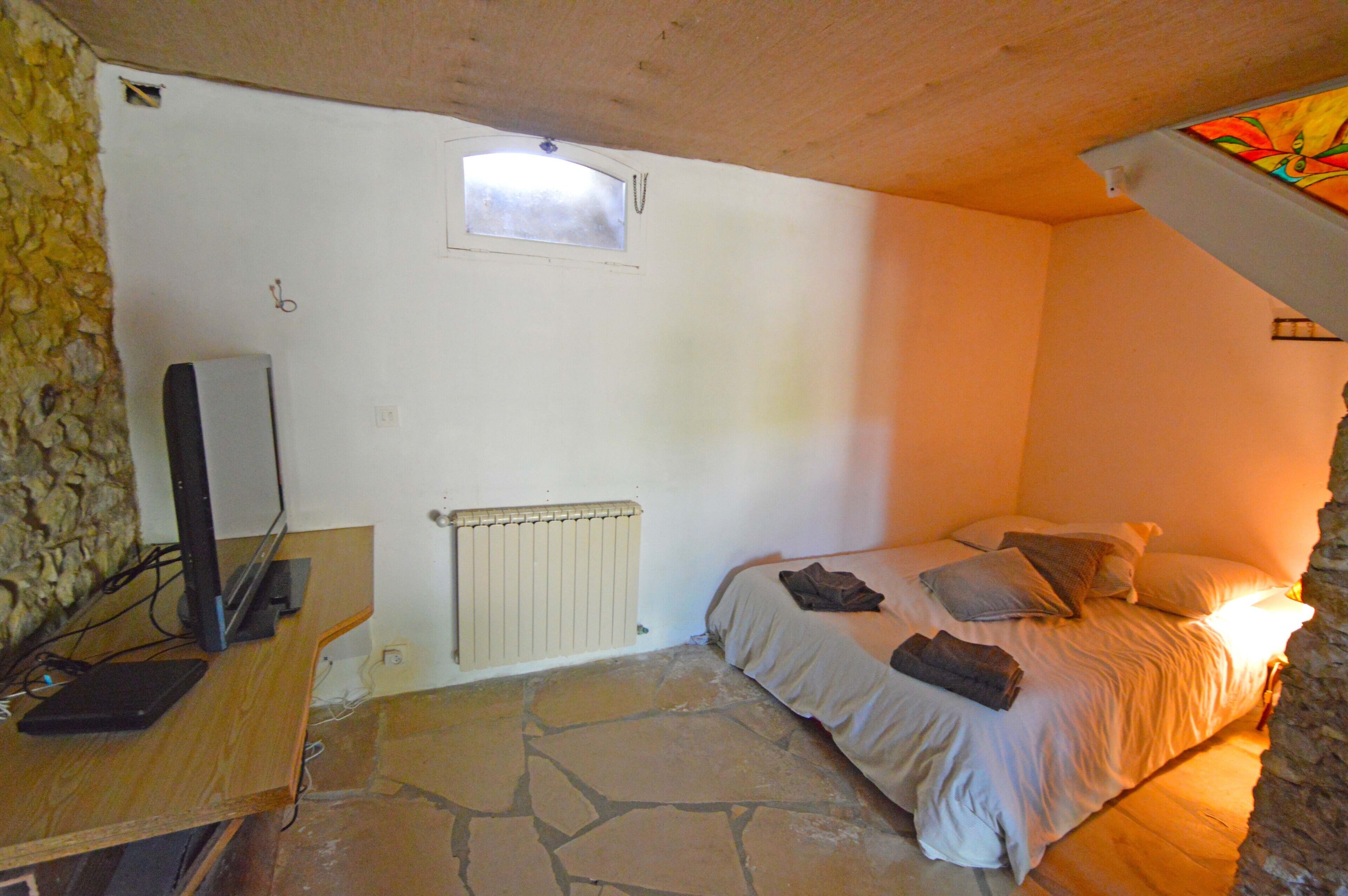 Un dormitorio con suelo de piedra, una cama con almohadas, un escritorio con computadora y una ventana.