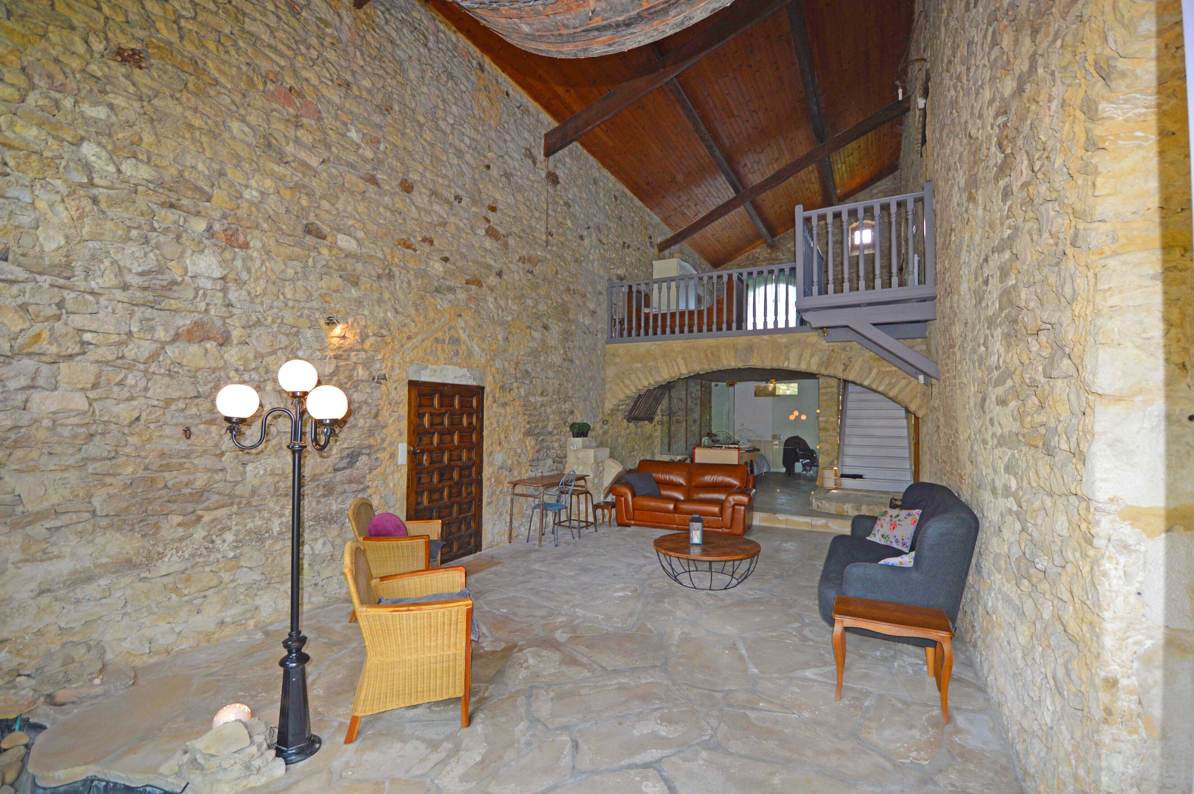 A stone-walled interior with a high ceiling, a balcony, wicker furniture, and a stone floor.