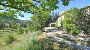 Un sendero rural que conduce a un edificio de piedra con un arco rústico, rodeado de vegetación exuberante y un paisaje montañoso.