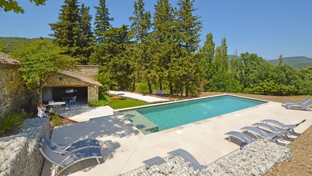 Una piscina con sillas de descanso, un edificio de piedra y un paisaje selvático.